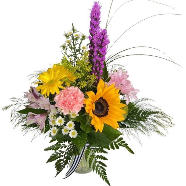 Mixed bouquet with sunflower, pink carnation, alstroemeria, chamomile, and tall purple liatris in a clear glass vase.