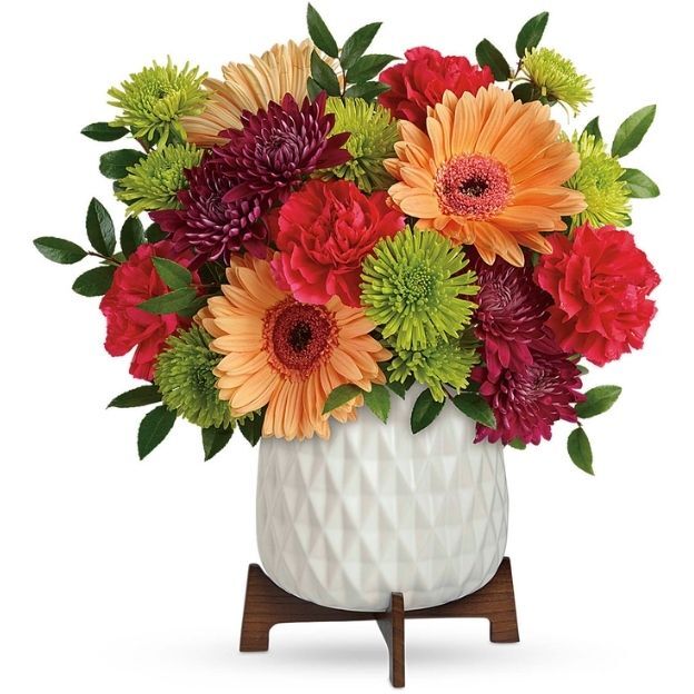 Colorful flower arrangement with gerbera daisies, carnations, and mums in a white textured vase.