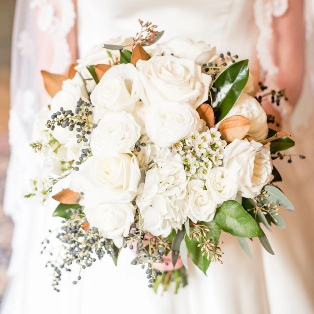 Close-up of a white bridal bouquet featuring roses, hydrangeas, greenery, and soft brown foliage.