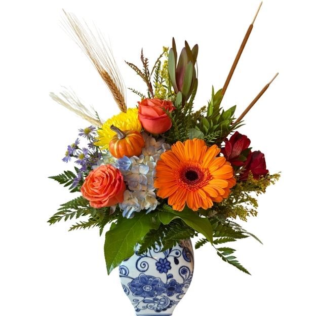 Blue-and-white vase with orange gerbera, roses, yellow mum, blue hydrangea, mini pumpkin, wheat, cattails, and greenery.