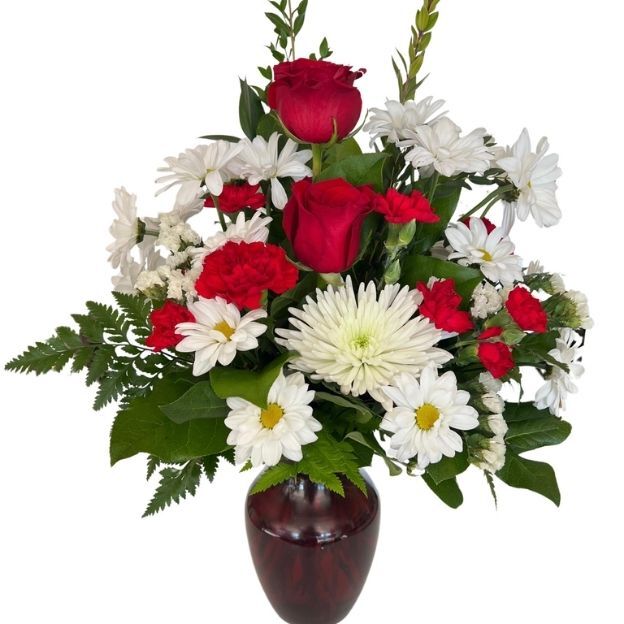 Red roses and carnations with white daisies and a spider mum, arranged with greenery in a dark red vase.