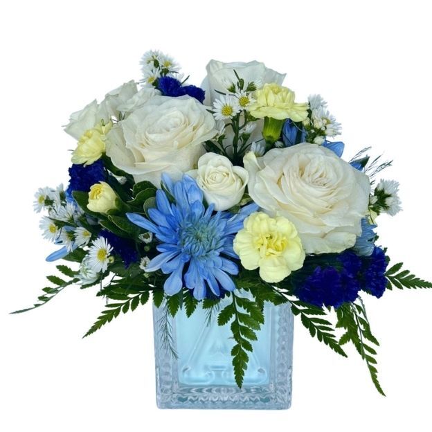 Blue and white bouquet with roses, blue chrysanthemums, yellow carnations, and greens in a square glass vase.